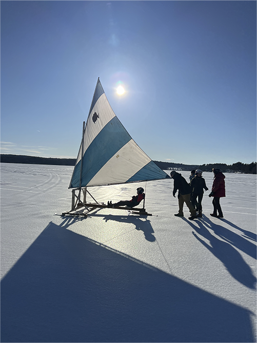 Scouts ice boating on a frozen lake under bright sun.